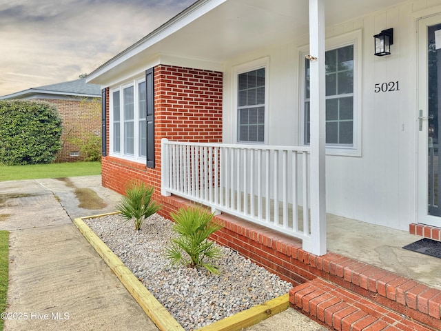 view of exterior entry featuring a porch and brick siding