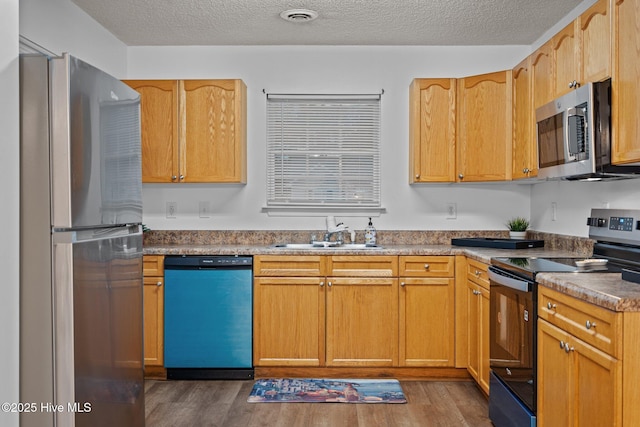 kitchen featuring stainless steel appliances, wood finished floors, a sink, and visible vents