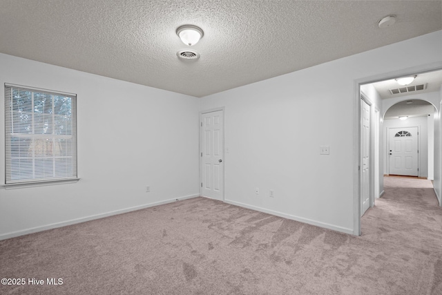 carpeted empty room featuring arched walkways, visible vents, a textured ceiling, and baseboards