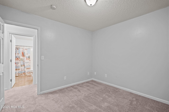 unfurnished room with light carpet, baseboards, and a textured ceiling