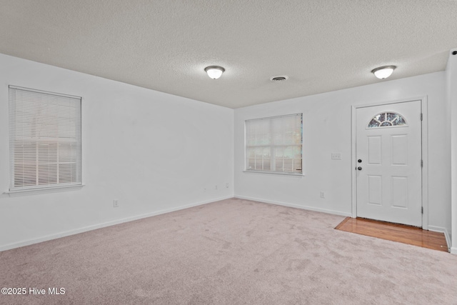 foyer featuring baseboards, a textured ceiling, visible vents, and carpet flooring