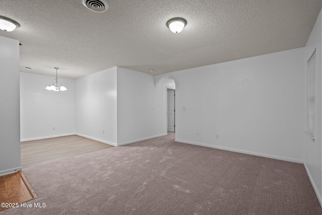 carpeted empty room with arched walkways, baseboards, visible vents, and an inviting chandelier