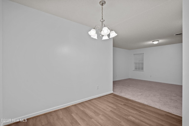 empty room featuring a chandelier, a textured ceiling, wood finished floors, visible vents, and baseboards