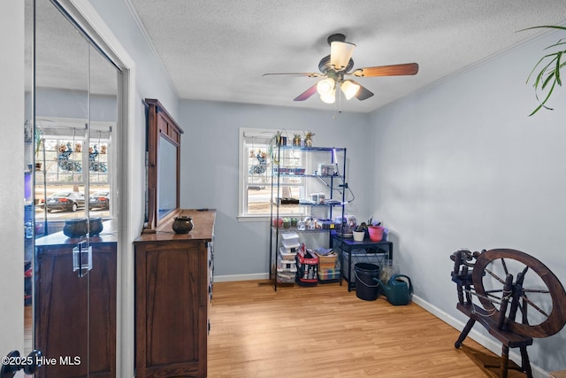 interior space featuring a ceiling fan, a textured ceiling, baseboards, and wood finished floors