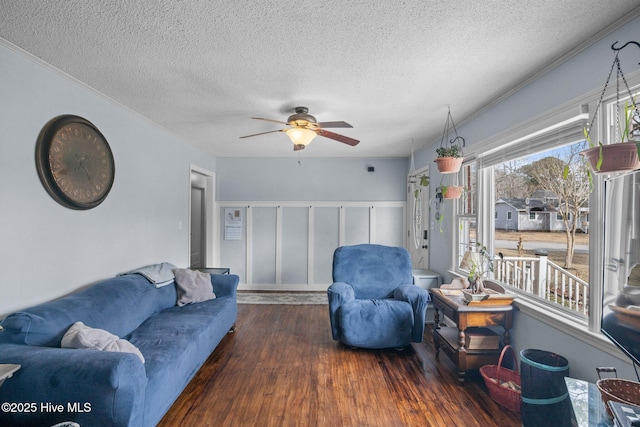 living room featuring ceiling fan, a textured ceiling, ornamental molding, and wood finished floors