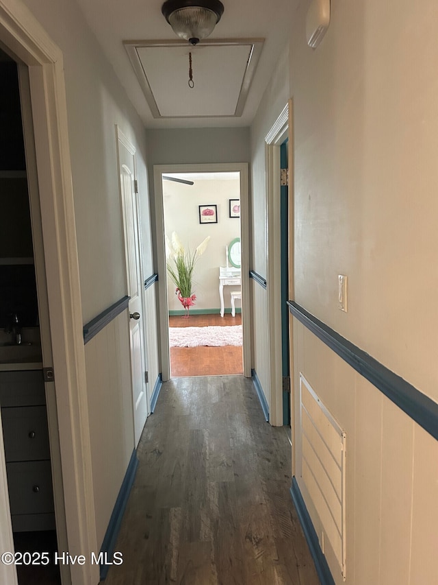 hall with attic access, dark wood-style flooring, and a wainscoted wall