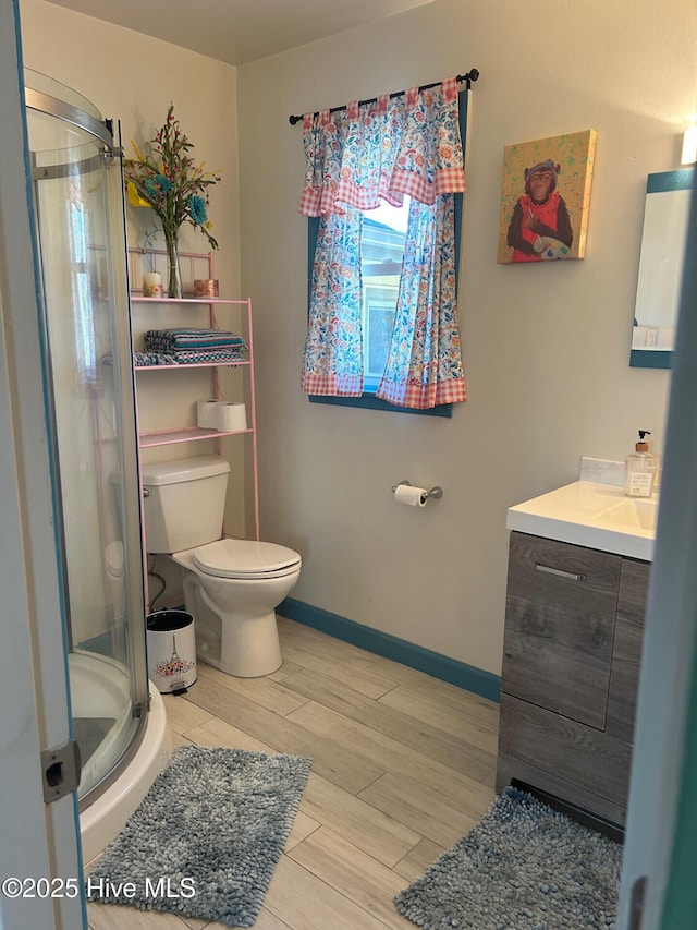 full bath featuring toilet, wood finished floors, vanity, baseboards, and a shower stall