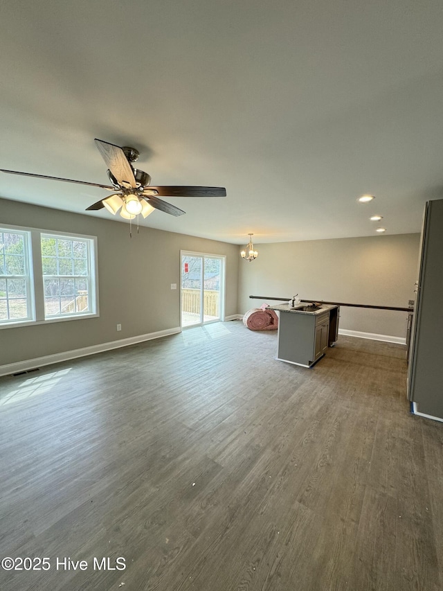 unfurnished living room with visible vents, ceiling fan with notable chandelier, dark wood-style flooring, and baseboards