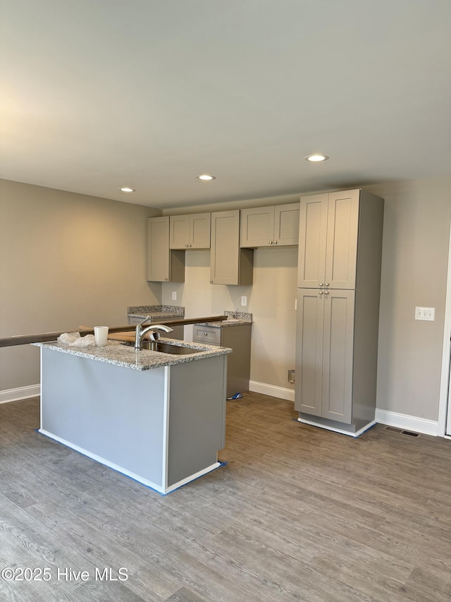 kitchen featuring gray cabinetry, a center island with sink, wood finished floors, recessed lighting, and baseboards