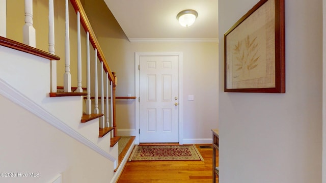 entryway featuring crown molding, visible vents, wood finished floors, baseboards, and stairs