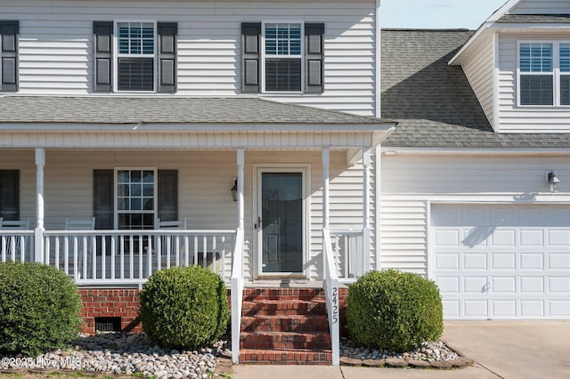 view of exterior entry with a garage, driveway, a porch, and a shingled roof