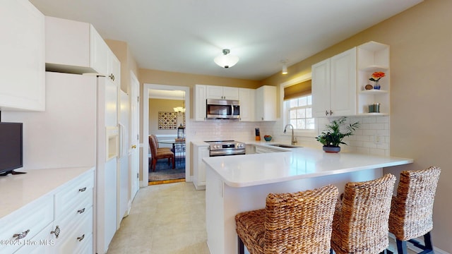 kitchen with light countertops, decorative backsplash, appliances with stainless steel finishes, a sink, and a peninsula