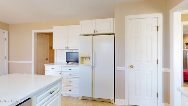 kitchen with white refrigerator with ice dispenser, backsplash, and white cabinetry