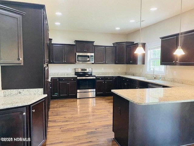 kitchen with wood finished floors, hanging light fixtures, appliances with stainless steel finishes, a sink, and light stone countertops