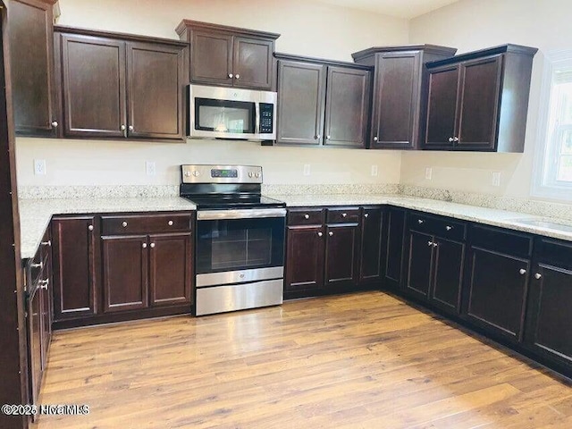 kitchen featuring light wood finished floors, light stone counters, stainless steel appliances, and dark brown cabinets