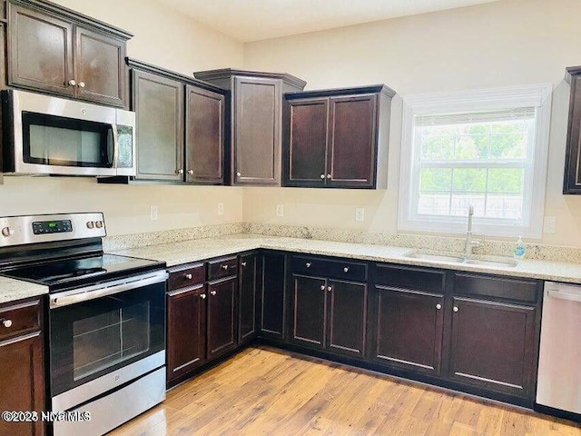 kitchen with stainless steel appliances, light wood-style flooring, a sink, dark brown cabinets, and light stone countertops