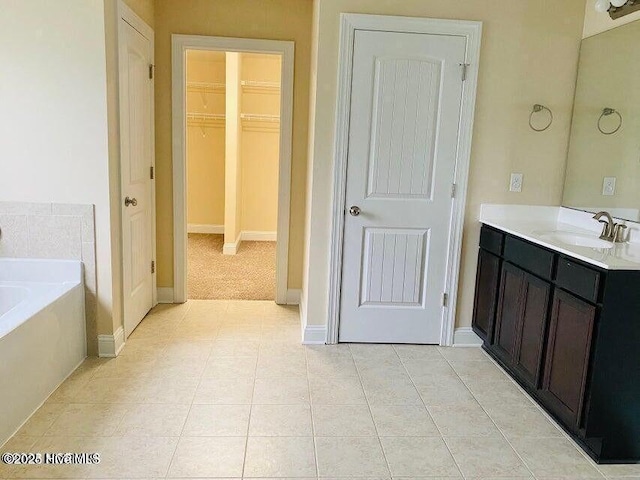 full bathroom with vanity, baseboards, a spacious closet, a bath, and tile patterned floors