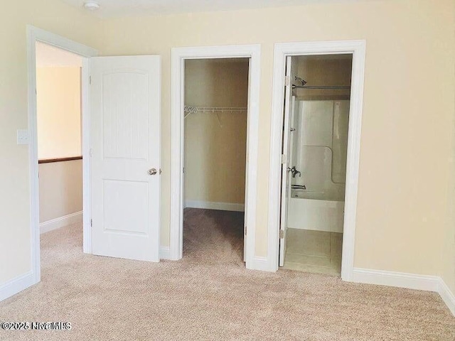 unfurnished bedroom with connected bathroom, carpet floors, baseboards, a closet, and a walk in closet