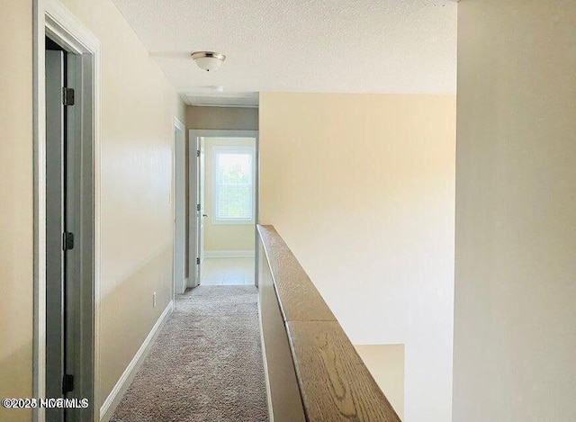 hallway with a textured ceiling, carpet, an upstairs landing, and baseboards