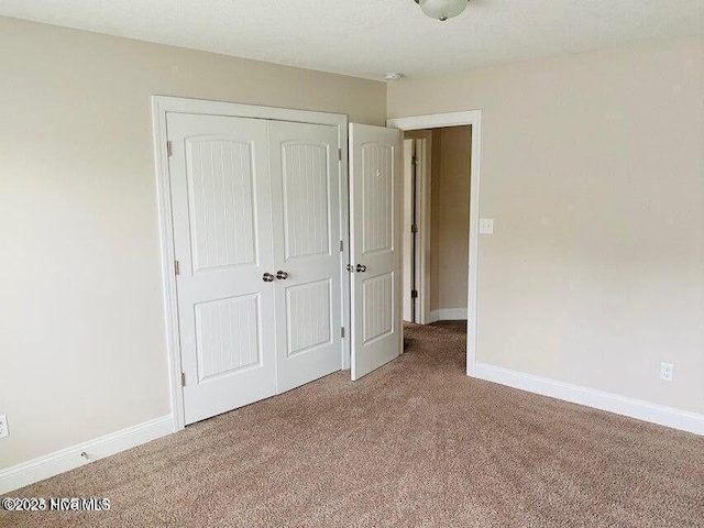 unfurnished bedroom featuring baseboards, a closet, and light colored carpet