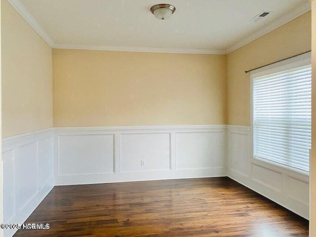 empty room with visible vents, wainscoting, ornamental molding, wood finished floors, and a decorative wall