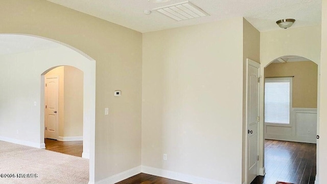 empty room with arched walkways, visible vents, dark wood finished floors, and baseboards