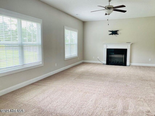 unfurnished living room featuring a fireplace with flush hearth, carpet, baseboards, and a ceiling fan