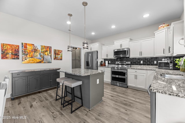 kitchen with stainless steel appliances, tasteful backsplash, light wood-style flooring, a kitchen island, and a sink