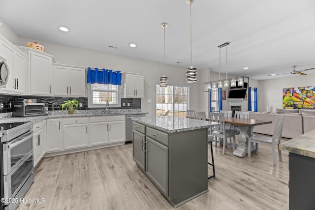 kitchen featuring decorative backsplash, appliances with stainless steel finishes, white cabinetry, a kitchen island, and light wood-type flooring