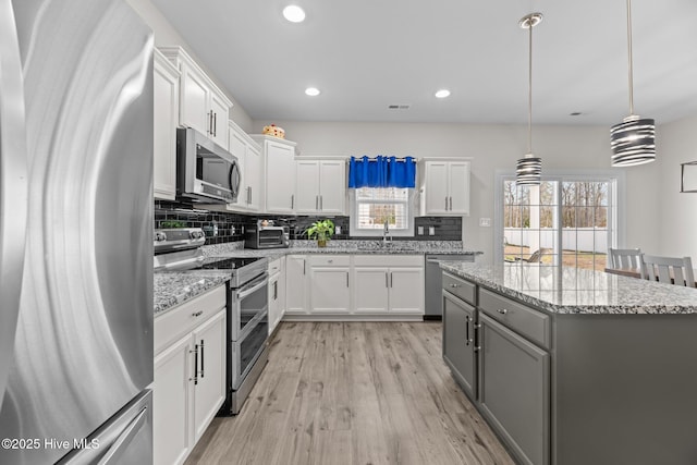 kitchen with white cabinets, a kitchen island, appliances with stainless steel finishes, light wood-type flooring, and backsplash