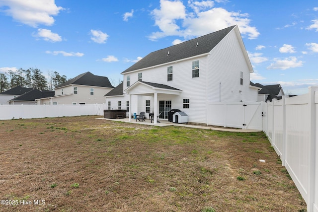 back of house with a hot tub, a lawn, a patio, a fenced backyard, and a gate