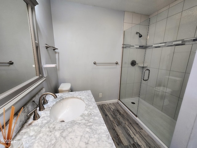 bathroom with toilet, a stall shower, wood finished floors, baseboards, and vanity