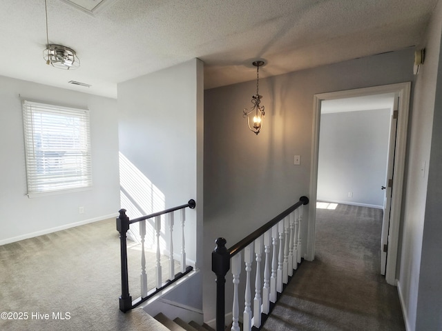 stairway featuring baseboards, visible vents, a textured ceiling, and carpet