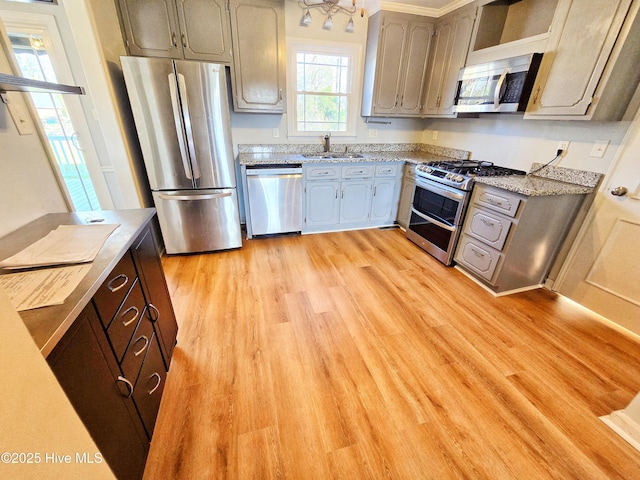 kitchen featuring light wood finished floors, stainless steel appliances, light stone counters, and a sink