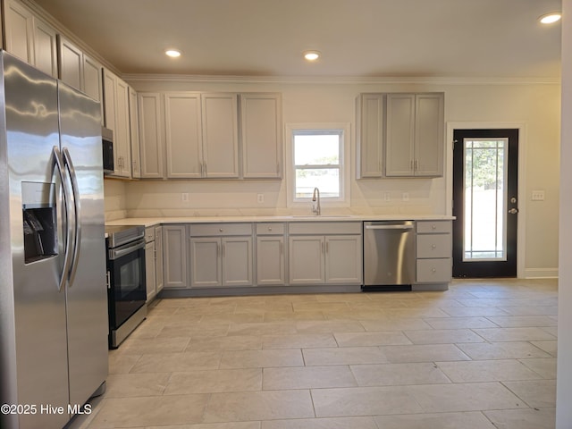 kitchen featuring gray cabinetry, a sink, appliances with stainless steel finishes, crown molding, and light countertops