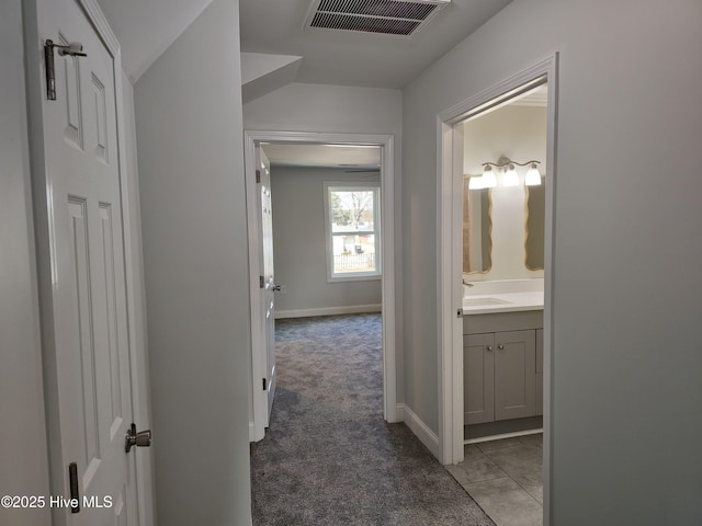 corridor featuring visible vents, carpet floors, baseboards, and a sink