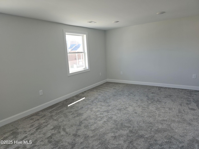 unfurnished room featuring visible vents, baseboards, and dark carpet