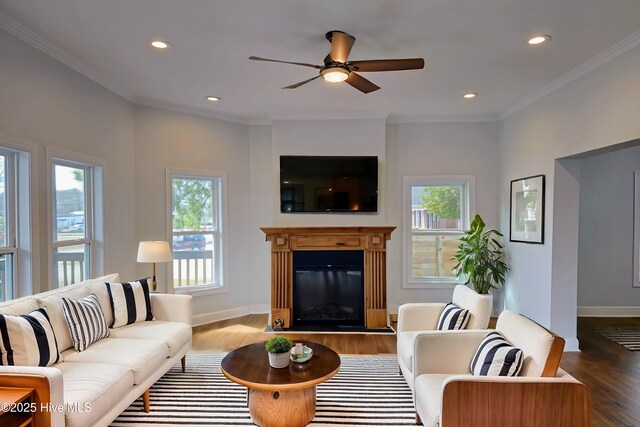 living room with wood finished floors, baseboards, recessed lighting, a glass covered fireplace, and crown molding