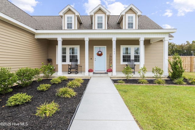 view of exterior entry with a shingled roof, covered porch, a yard, and fence