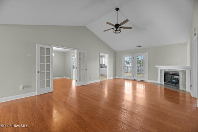 unfurnished living room featuring baseboards, a tiled fireplace, a ceiling fan, wood finished floors, and french doors