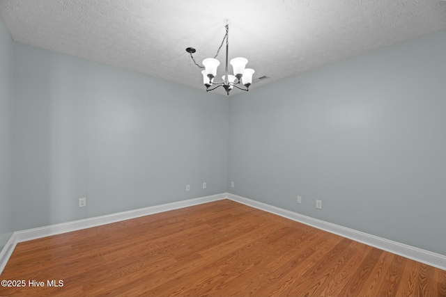 unfurnished room featuring a chandelier, a textured ceiling, baseboards, and wood finished floors