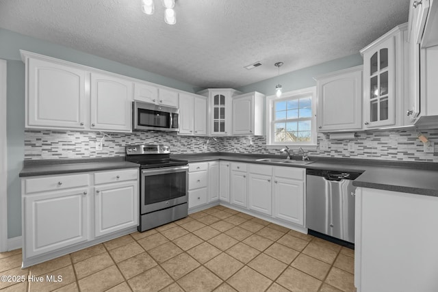 kitchen with appliances with stainless steel finishes, dark countertops, a sink, and glass insert cabinets