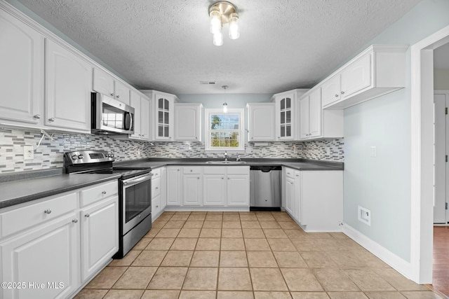 kitchen featuring stainless steel appliances, dark countertops, glass insert cabinets, and white cabinetry