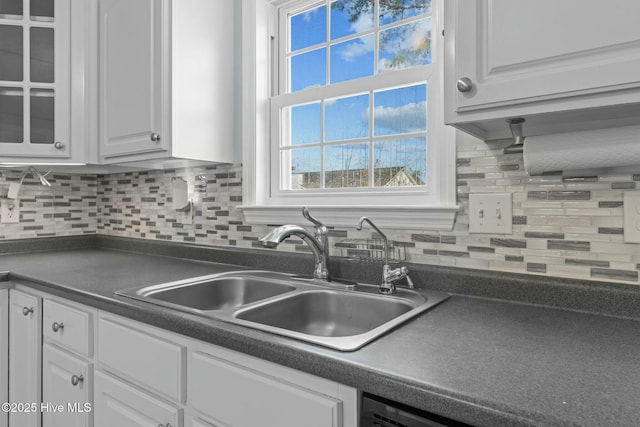 kitchen with dark countertops, white cabinetry, a sink, and decorative backsplash