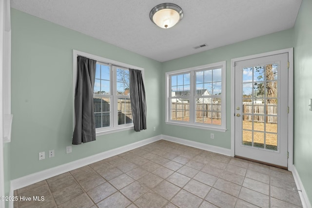 empty room featuring baseboards, visible vents, a textured ceiling, and tile patterned floors