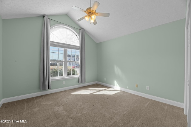 carpeted spare room with lofted ceiling, ceiling fan, baseboards, and a textured ceiling