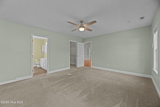 unfurnished bedroom featuring a walk in closet, a closet, visible vents, carpet flooring, and baseboards