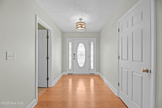 foyer entrance featuring a textured ceiling, baseboards, a notable chandelier, and light wood-style floors