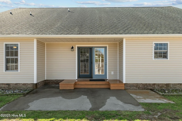 view of exterior entry with a patio and a shingled roof