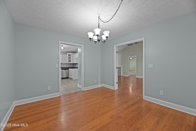 unfurnished dining area featuring light wood-type flooring, a textured ceiling, baseboards, and a notable chandelier